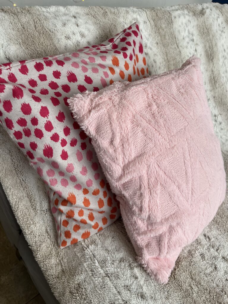 Pink and orange patterned cushion covers styled with a blush pink pillow